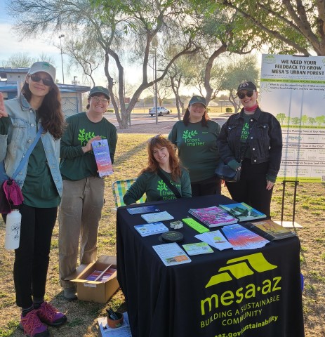 Five people wearing Trees Matter shirts gathered around a table with a Mesa AZ tablecloth and handouts on top.
